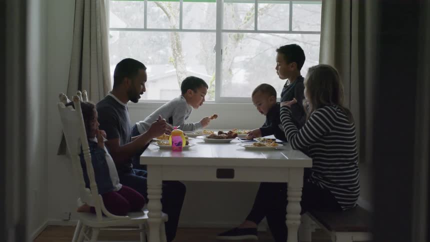 A family sits at a table near a window in their home eating a meal together