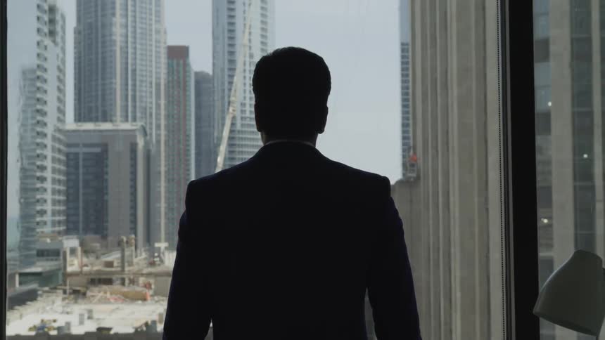 A man in a suit looking out of the window at the many skyscrapers in a city