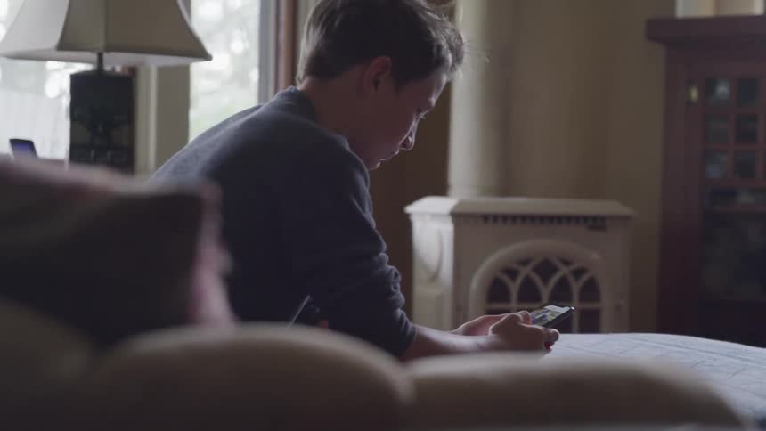 A young boy sits and uses his cellphone