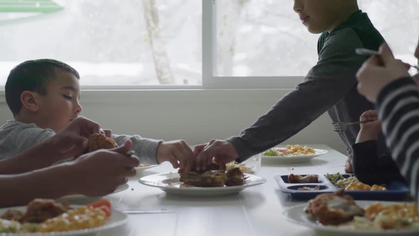 Two boys reach to grab food from a plate in the middle of a table