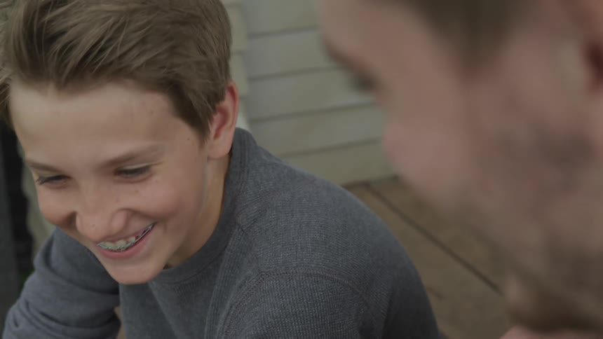 A boy and a man sitting on a porch talking and laughing