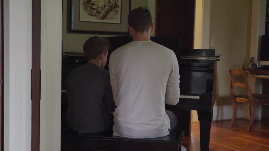 A young boy and a teenage boy are sitting at a piano playing together