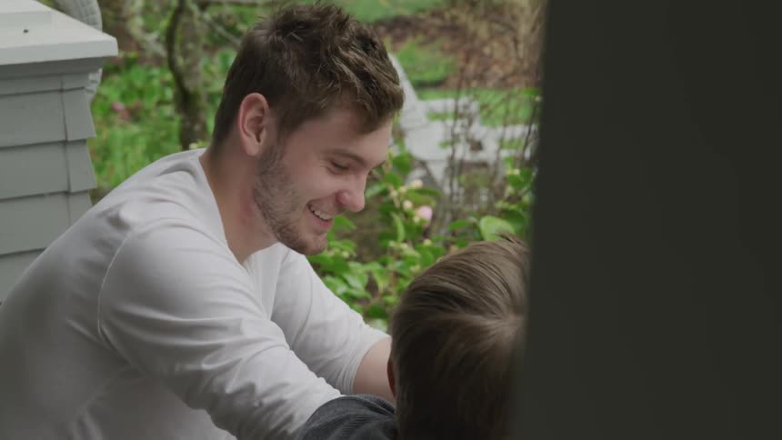 Man and boy sitting on a porch talking as the man gives the boy a smile and a hug