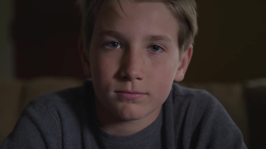 A boy sits leaning forward and staring straight ahead
