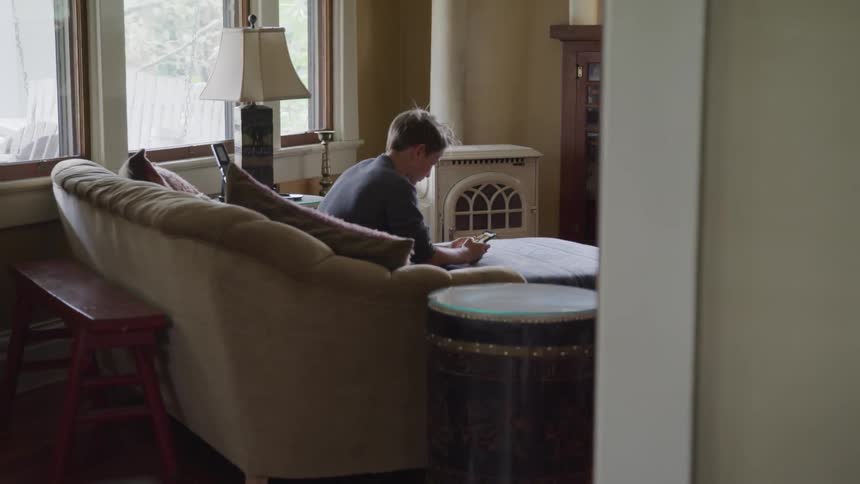 Man sits on couch scrolling through mobile phone