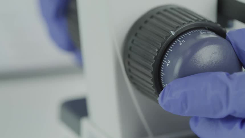 A person wearing gloves turns a dial on some equipment