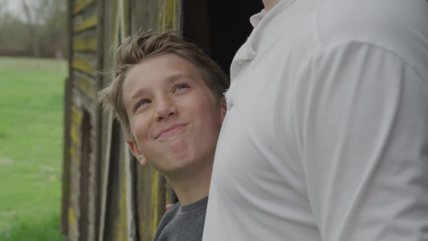 A boy standing in the doorway of a barn looking up at a man