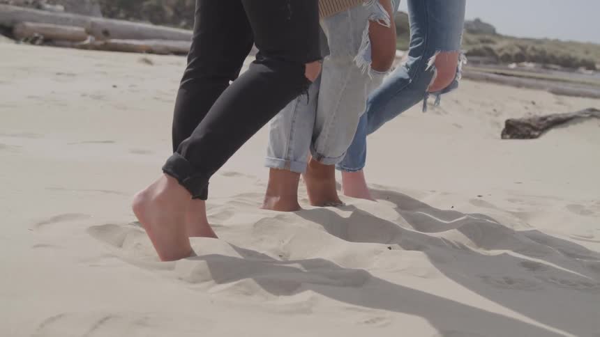 Three women stand together laughing and hugging on the beach