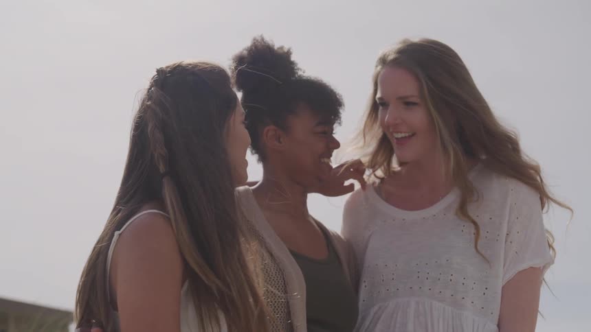 Three young women stand and talk and laugh