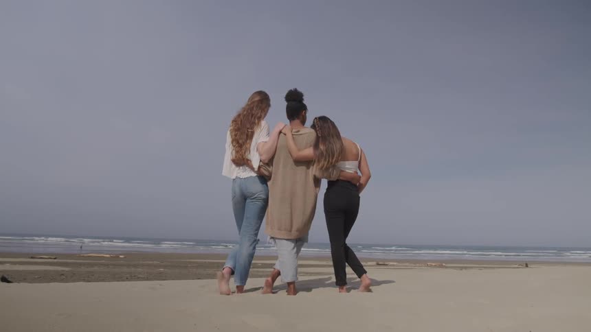 Three woman stand on the sand next to the ocean