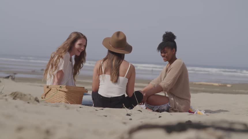 Three teenagers sit on the beach and laugh together