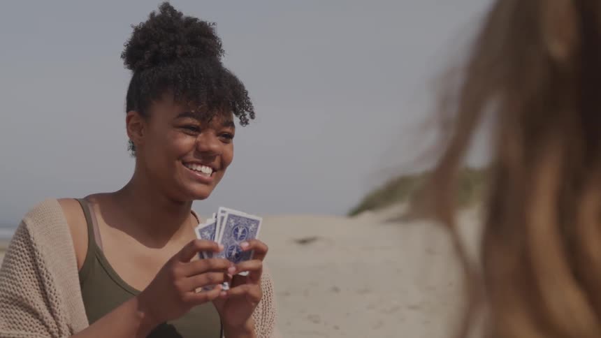 A group of girls play cards on the beach