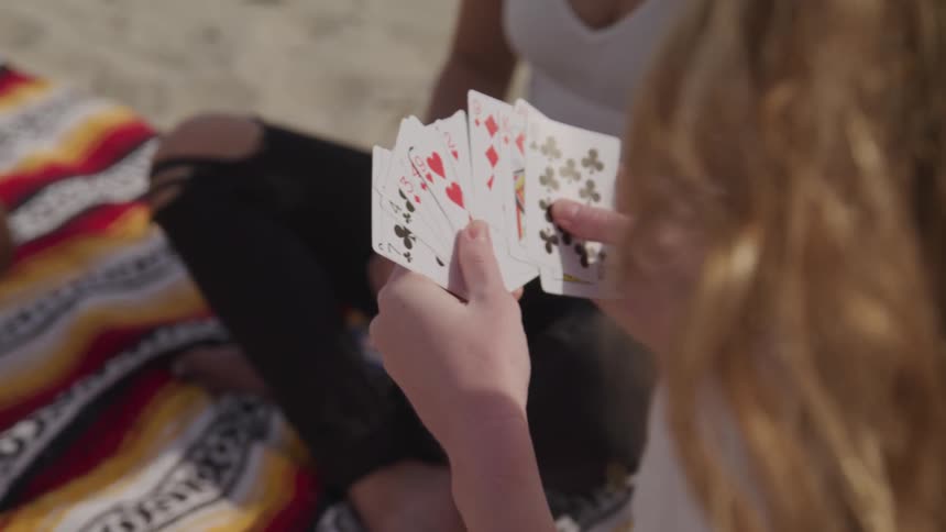 Women sitting on a beach blanket in the sand playing cards