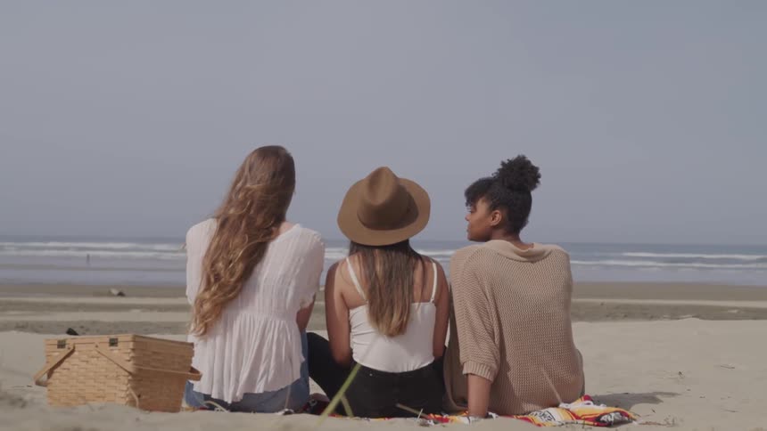 Three young women sit on the beach together