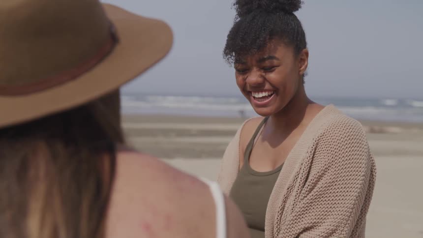 Two women are sitting outside and laughing by the beach