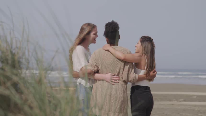 A group of friends embrace while standing and talking on a beach