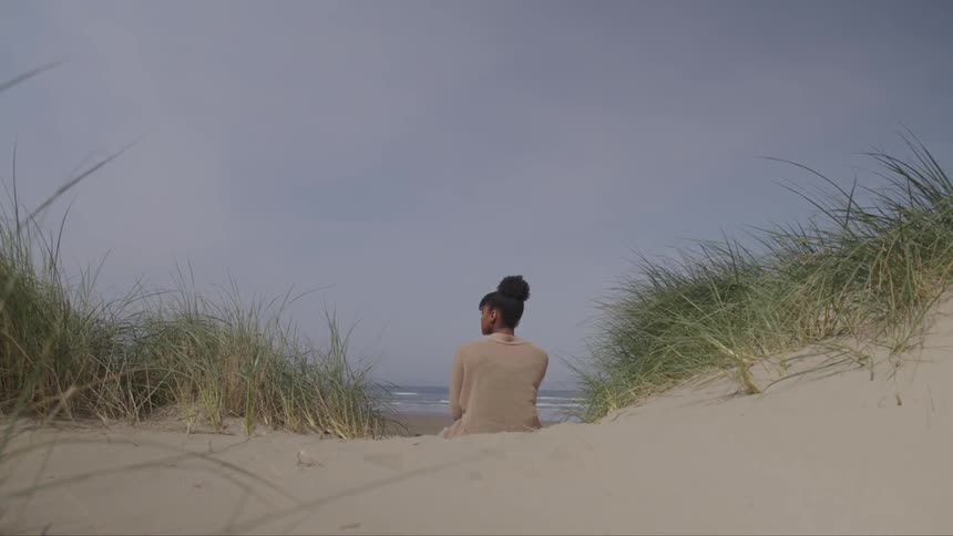 A woman sits on the sand looking at the ocean