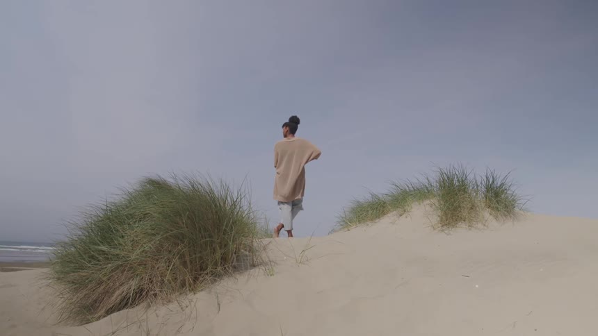 A woman stands on a sand dune near the ocean