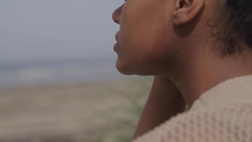 A woman is staring outdoors while wearing a sweater