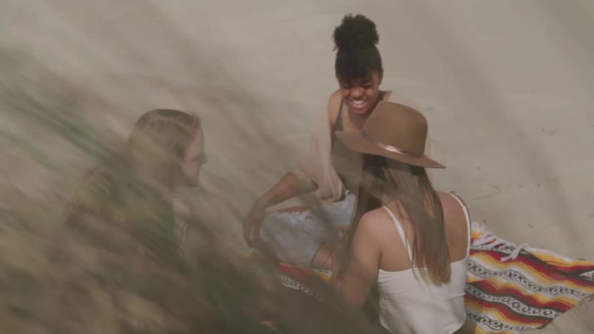 Female friends sitting on a blanket laughing while playing cards at the beach