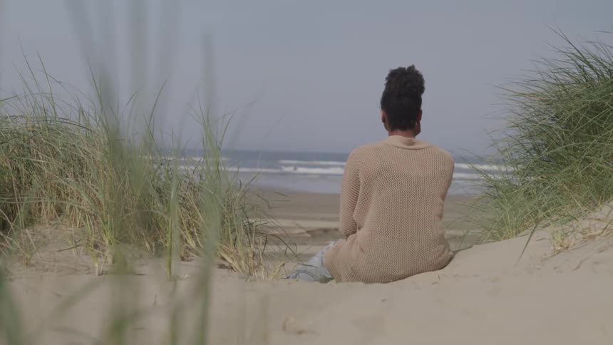 Woman sits in the sand near the weeds on the beach