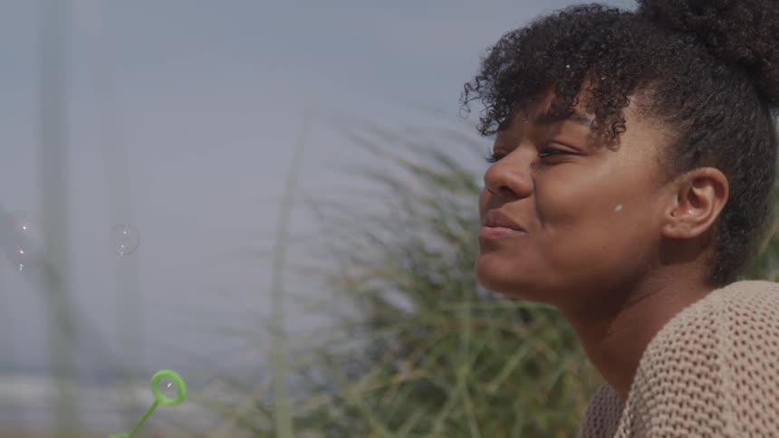 A young black girl blows bubbles outdoors