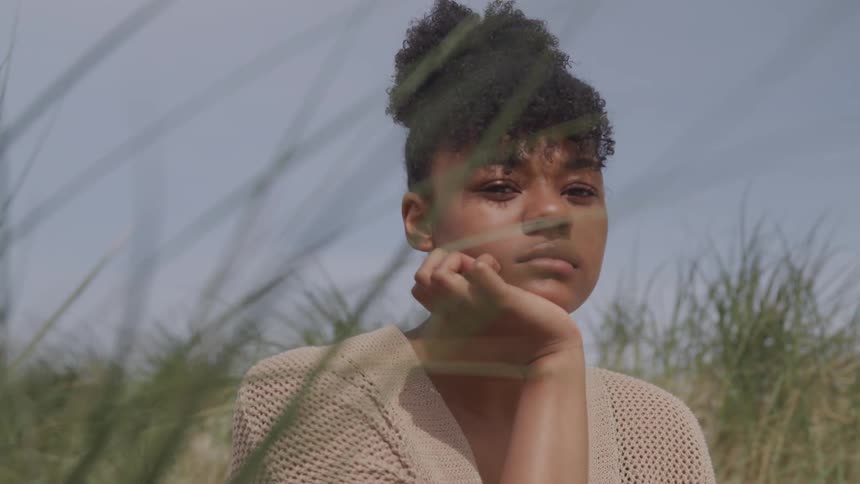 Black woman rests her chin on her hand on the beach during the daylight