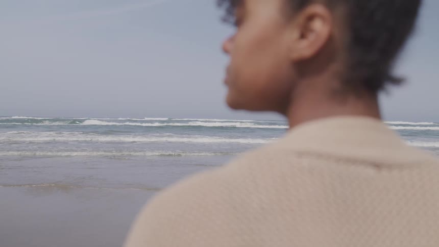 A black girl stands and looks out at the water