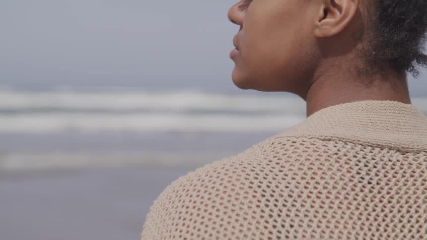 Woman stands looking across beach during the day