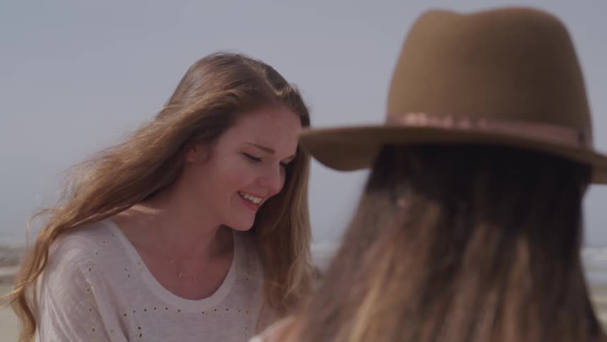 Two friends are smiling outdoors while sitting on the beach