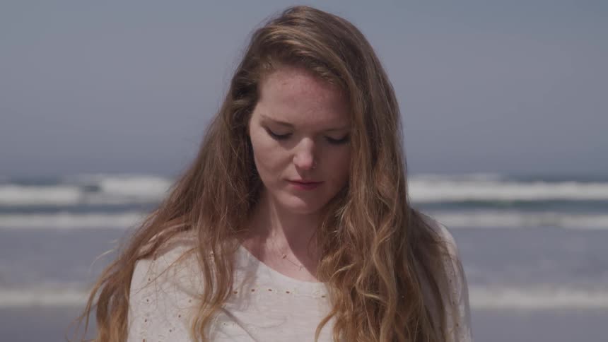 A young girl sits on the beach and looks down