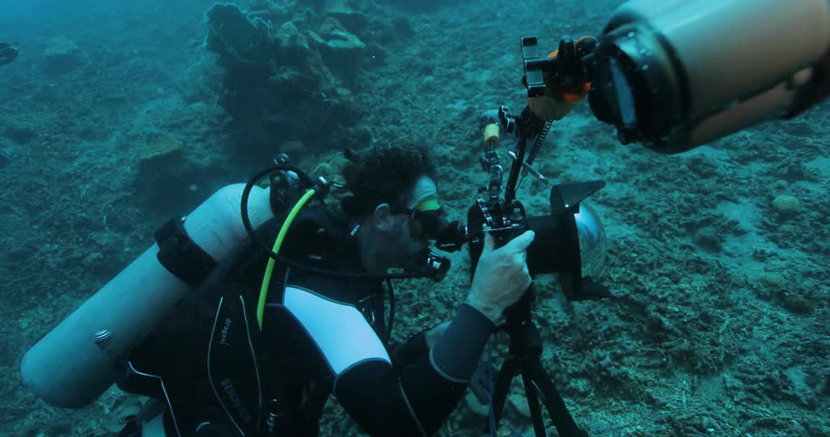 A scuba diver at the bottom of the ocean looking through a telescope