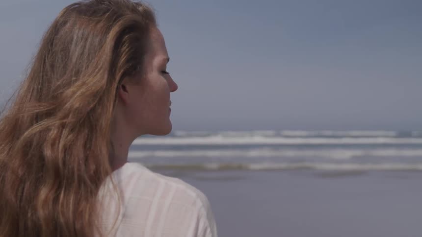 A woman at the beach with sandy colored hair has her eyes close