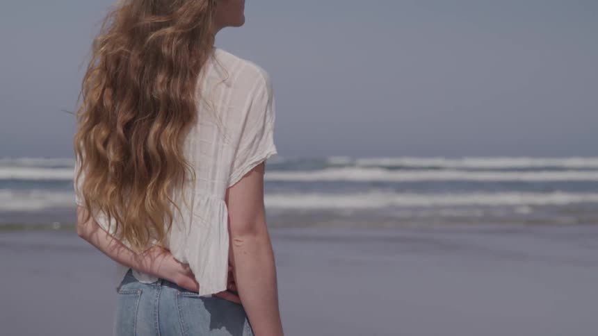 Blonde woman stands on the sand beach by seaside