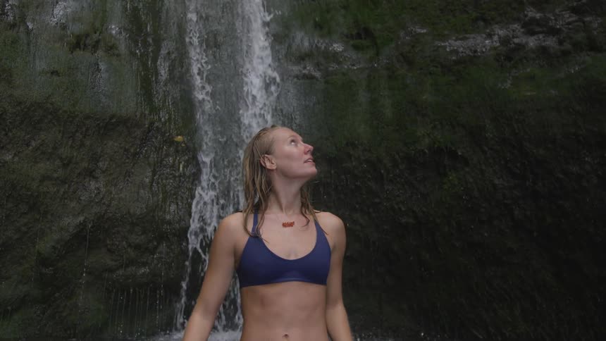 Woman in a bikini stands in the water near a waterfall