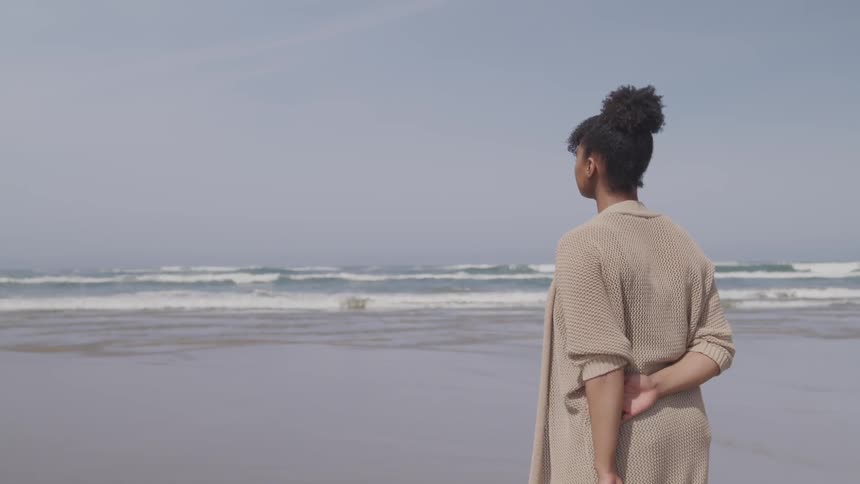 A woman stands by the coastline and stares to the ocean water