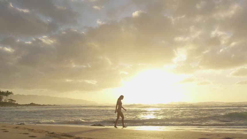 A woman in a bathing suit walks toward the ocean on an empty beach at sunset