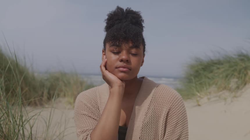 A young black woman sitting on a beach and turning her head to look at the camera