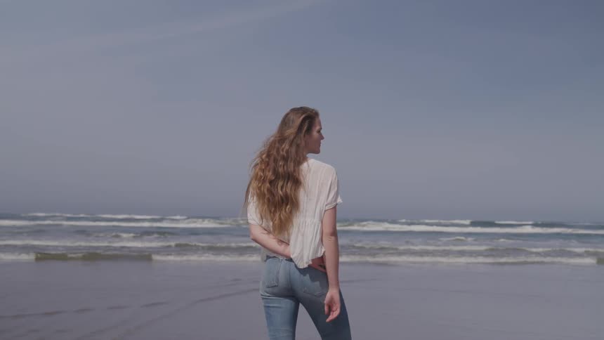 Woman stands on the wet sand beach and looks sideways next to the ocean