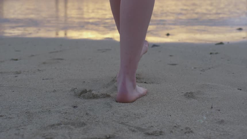 Woman walks toward surf leaving footprints in the sand