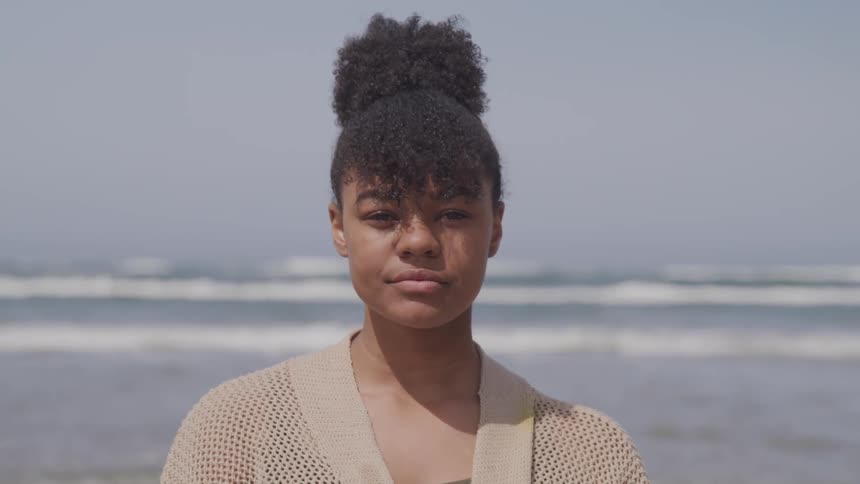 A woman in a sweater stands on a beach