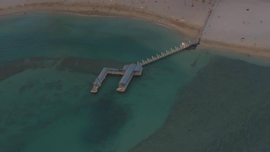 A dock juts out from the beach into clear ocean water