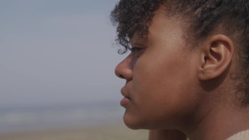 A girl standing up on the beach staring off into the distance