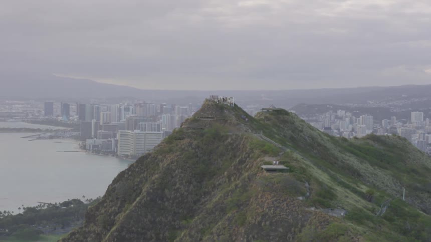 People stand on hill top observation decks overlooking a coastal city at sunset