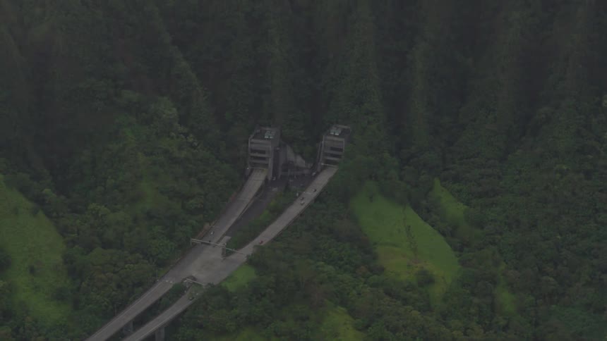 Cars traveling along two large freeways pass into and out of tunnels within the side of a mountain