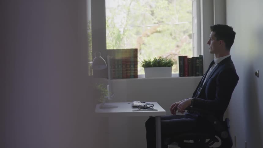 A man in a suit types on a keyboard and stops to look outside