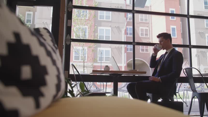 Businessman sitting at the table uses laptop and sips on a cup of coffee in the cafe