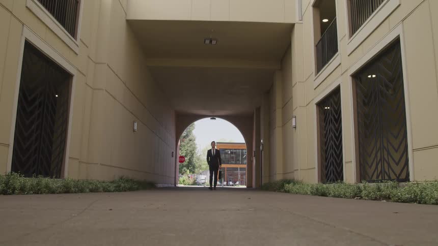 Business man carrying a briefcase walking through outdoor corridor of a building