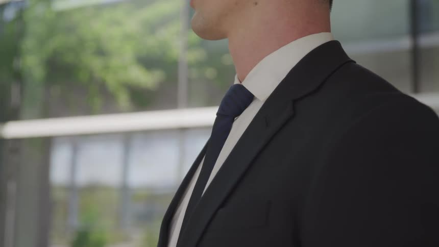 A man wearing a suit and tie stands near a building