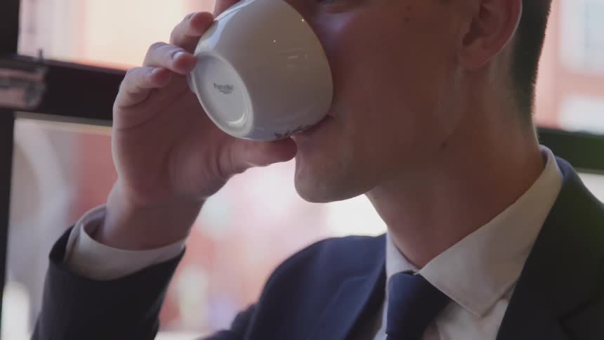 A young white man in a suit drinks from a coffee cup